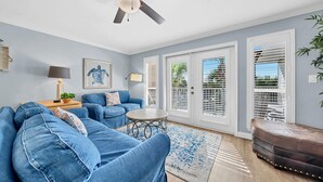 A living room with a blue sofa, a round coffee table, and a ceiling fan. - ☀️Beach-Pool Access-30A-Gulf Place Caribbean 311 (Santa Rosa Beach)
