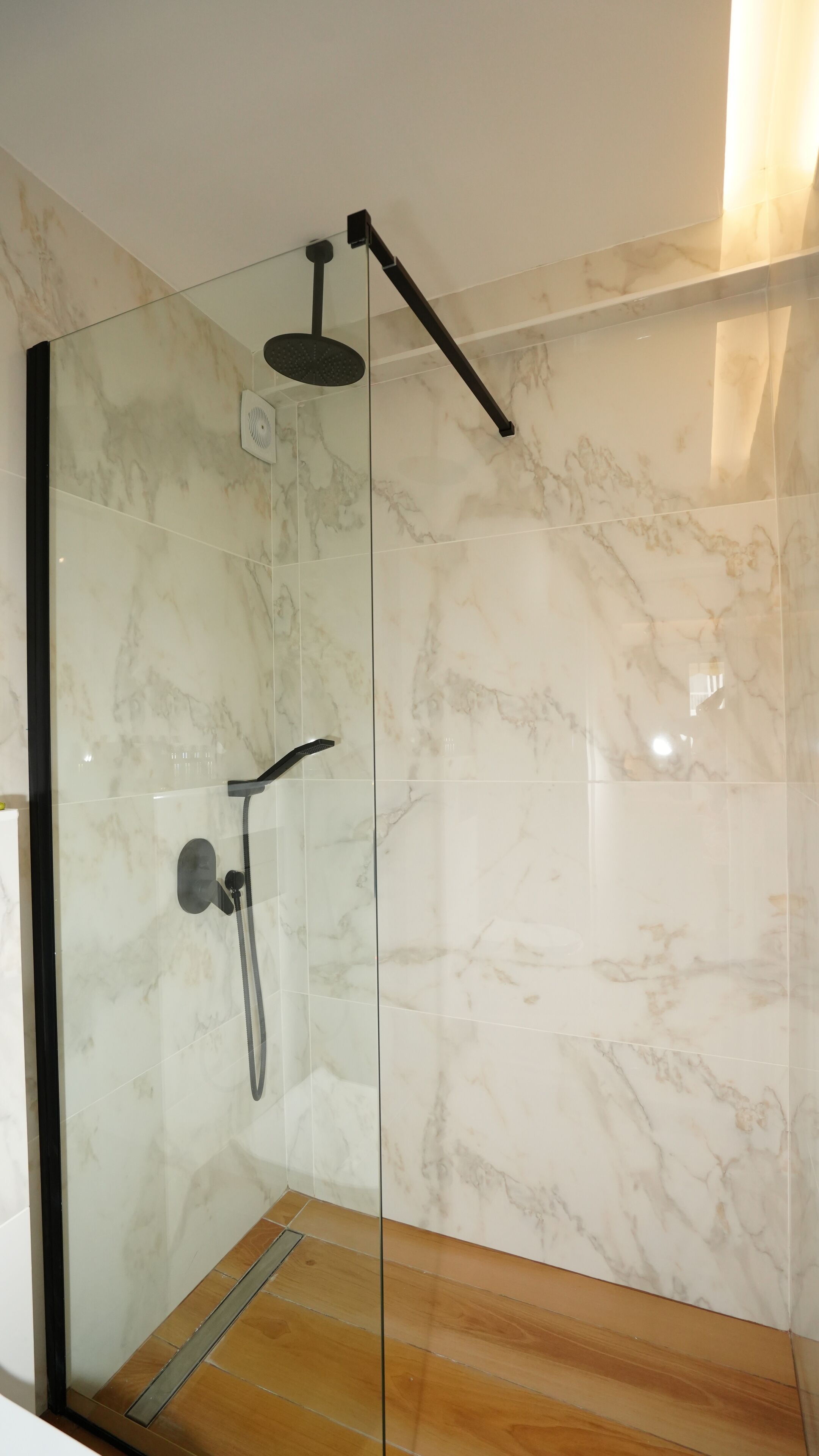 Una cabina doccia in vetro con soffione a mano e pannello comandi a parete.