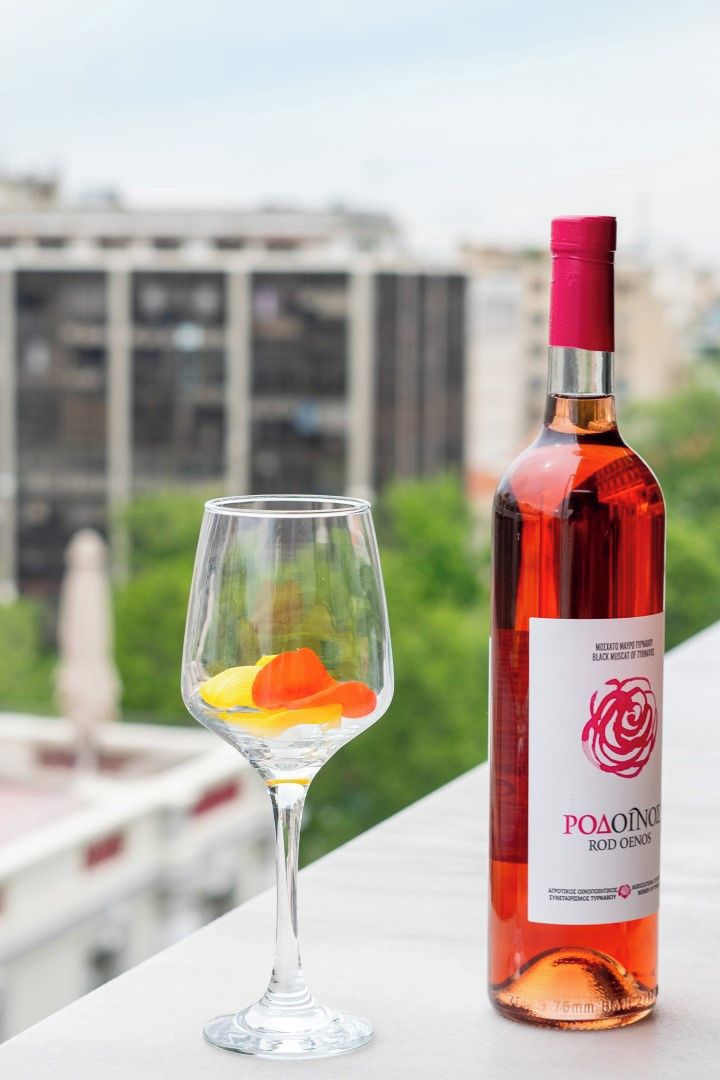 A bottle of red wine and a glass with fruit on a balcony with a cityscape in the background.