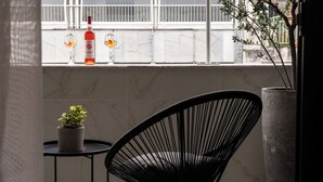 Een zwarte stoel, een klein tafeltje met een bloempot, en twee glazen met een fles op een balkonhek.