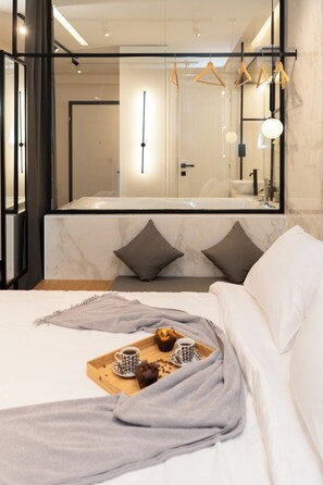 Camera d'albergo moderna con un letto grande, un vassoio di legno con prodotti per la colazione e uno specchio grande che riflette la stanza.