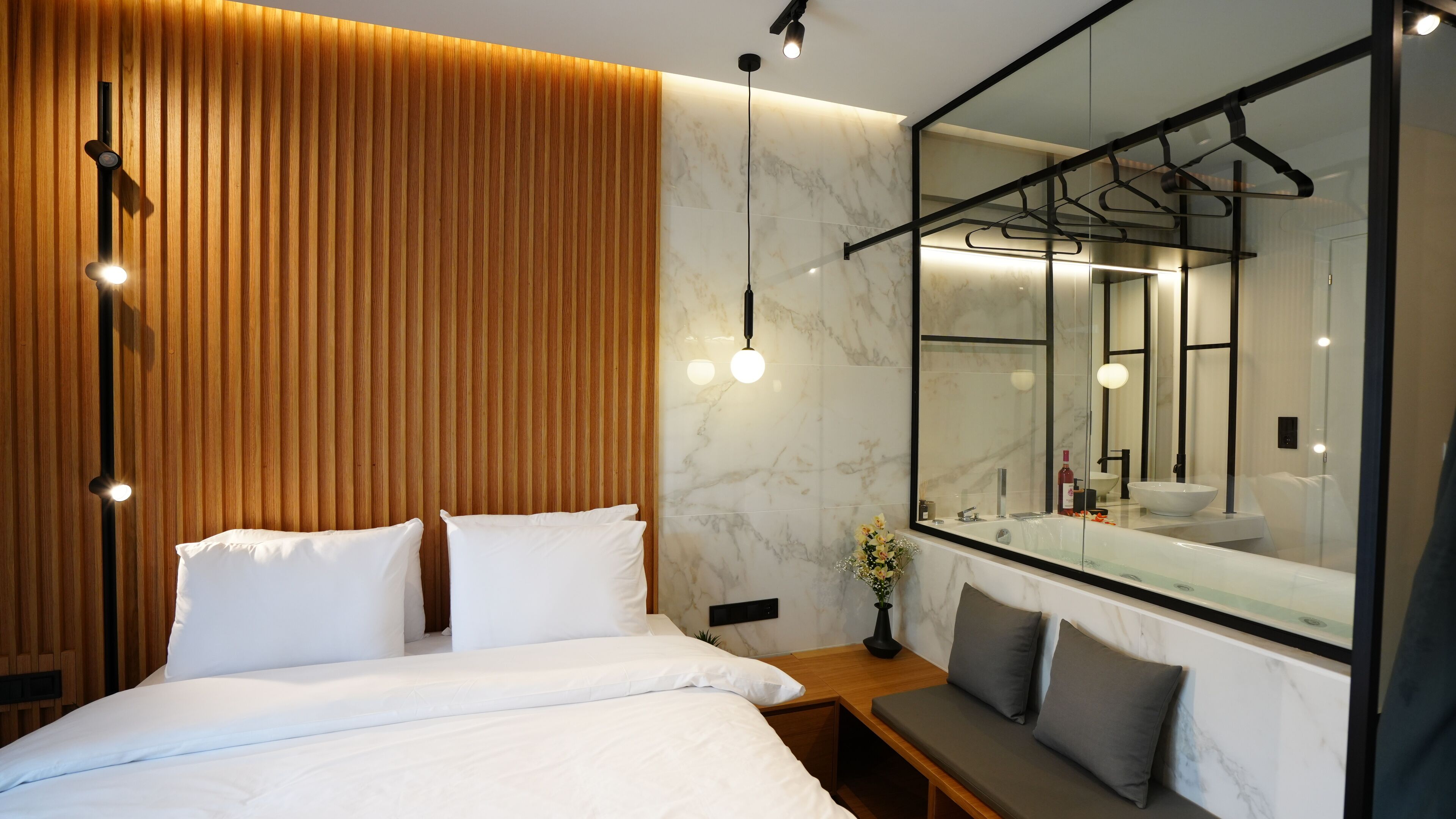 A modern bedroom with a large bed, a wooden accent wall, a marble bathroom with a large mirror, and pendant lighting.