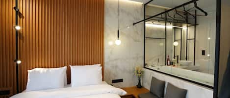 A modern bedroom with a large bed, a wooden accent wall, a marble bathroom with a large mirror, and pendant lighting.