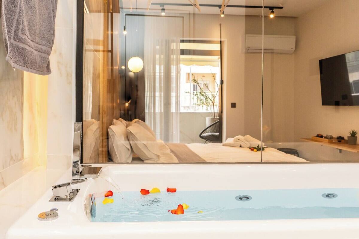 Een moderne badkamer met een ruime badkuip, een douchecabine met glazen wanden en een aan de muur bevestigde televisie.