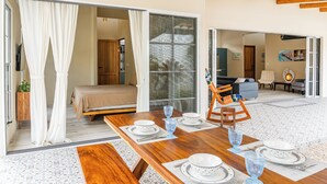 Ein Essbereich mit einem Holztisch, gedeckt für vier Personen, ein Bett mit Baldachin und Blick auf ein Wohnzimmer durch eine offene Tür.