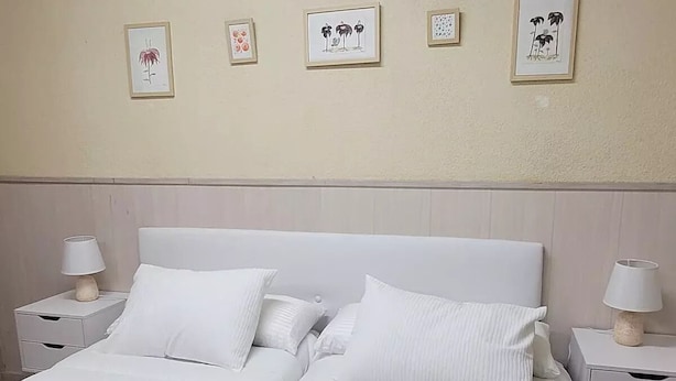 Una cama doble con ropa de cama blanca, dos mesitas de noche con lámparas y cuatro cuadros enmarcados en la pared.