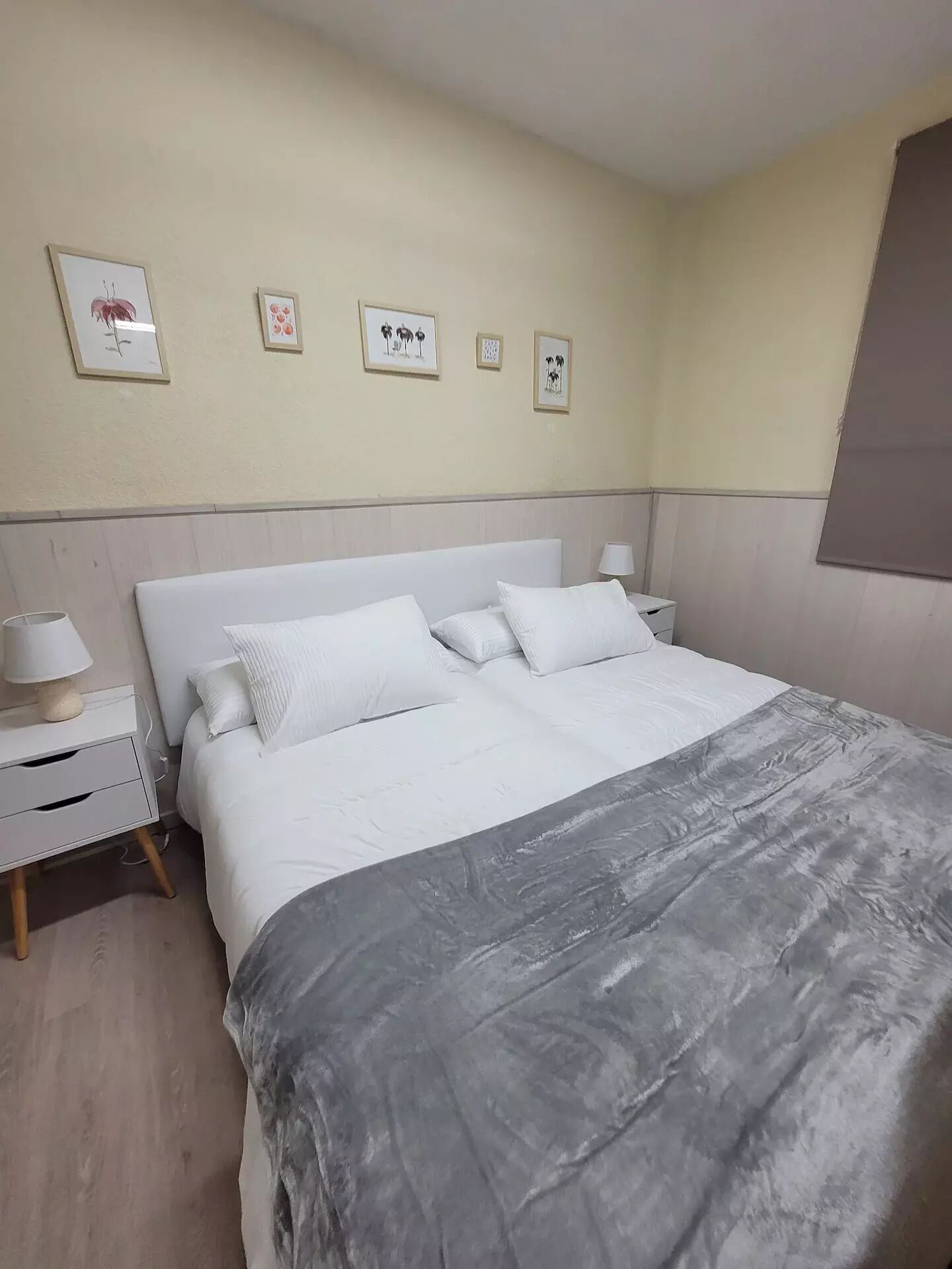 Un dormitorio con una cama grande, una mesita de noche con lámpara y tres cuadros en la pared.
