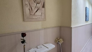 Un área de recepción con una obra de arte enmarcada, un florero con una rosa y una estantería blanca con documentos.