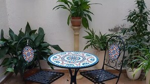 Un pequeño patio con una mesa y sillas de cerámica, rodeado de plantas en macetas.