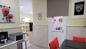 Cocina compacta con microondas, un basurero pequeño y un comedor con mesa de vidrio y sillas rojas.