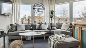 A modern living room with a grey sectional sofa, a round coffee table, and a large window offering a view of the outdoors. - Pensionat Enehall (Bastad)