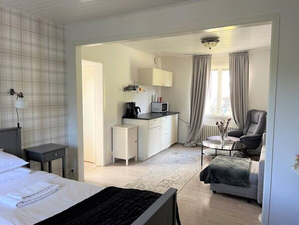A hotel room with a bed, a small desk, a kitchenette, a chair, and a sofa. - Pensionat Enehall (Bastad)