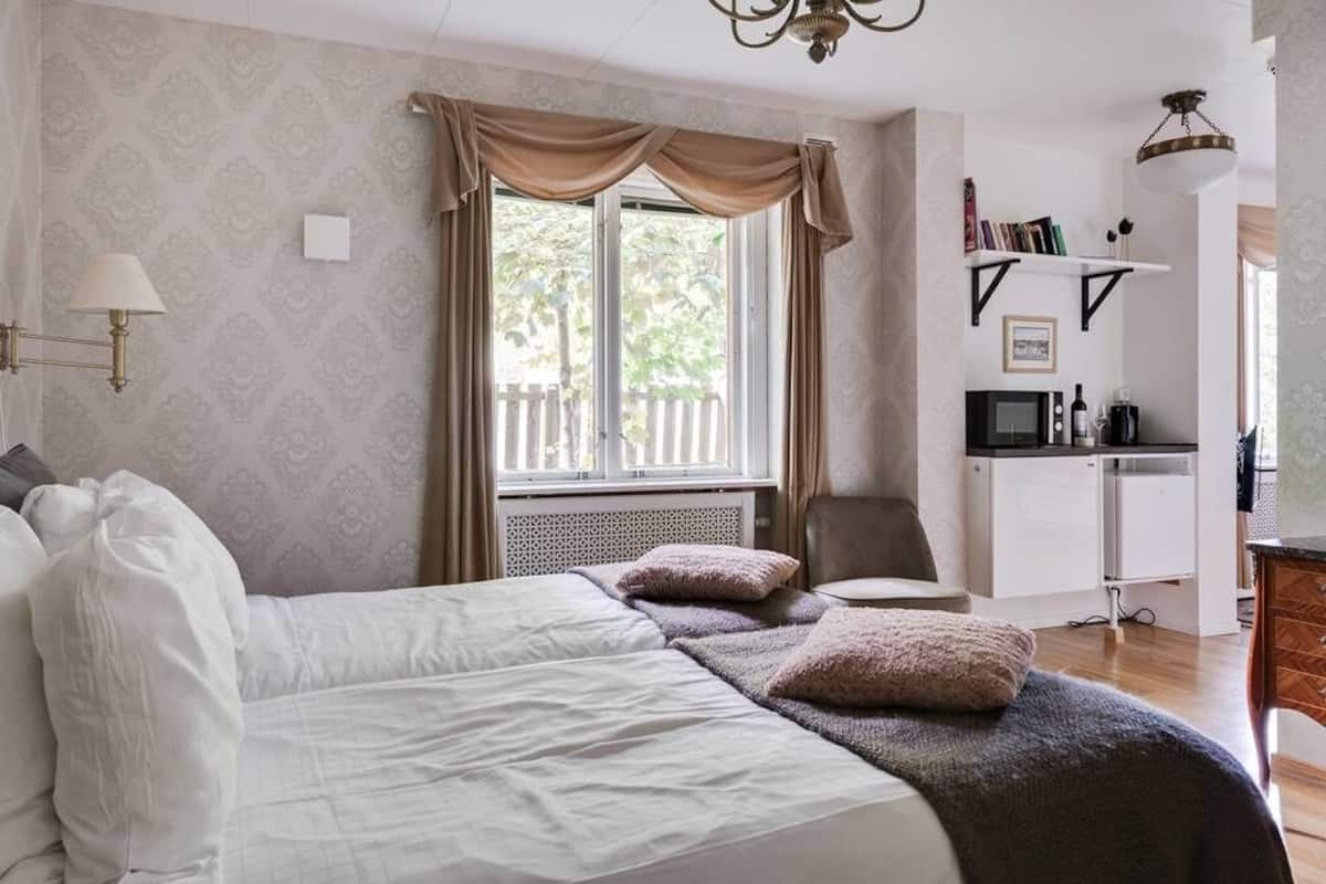 Ein Schlafzimmer mit einem Bett, einem Sessel, einem Schreibtisch mit Computer und einem Fenster mit Vorhängen.
