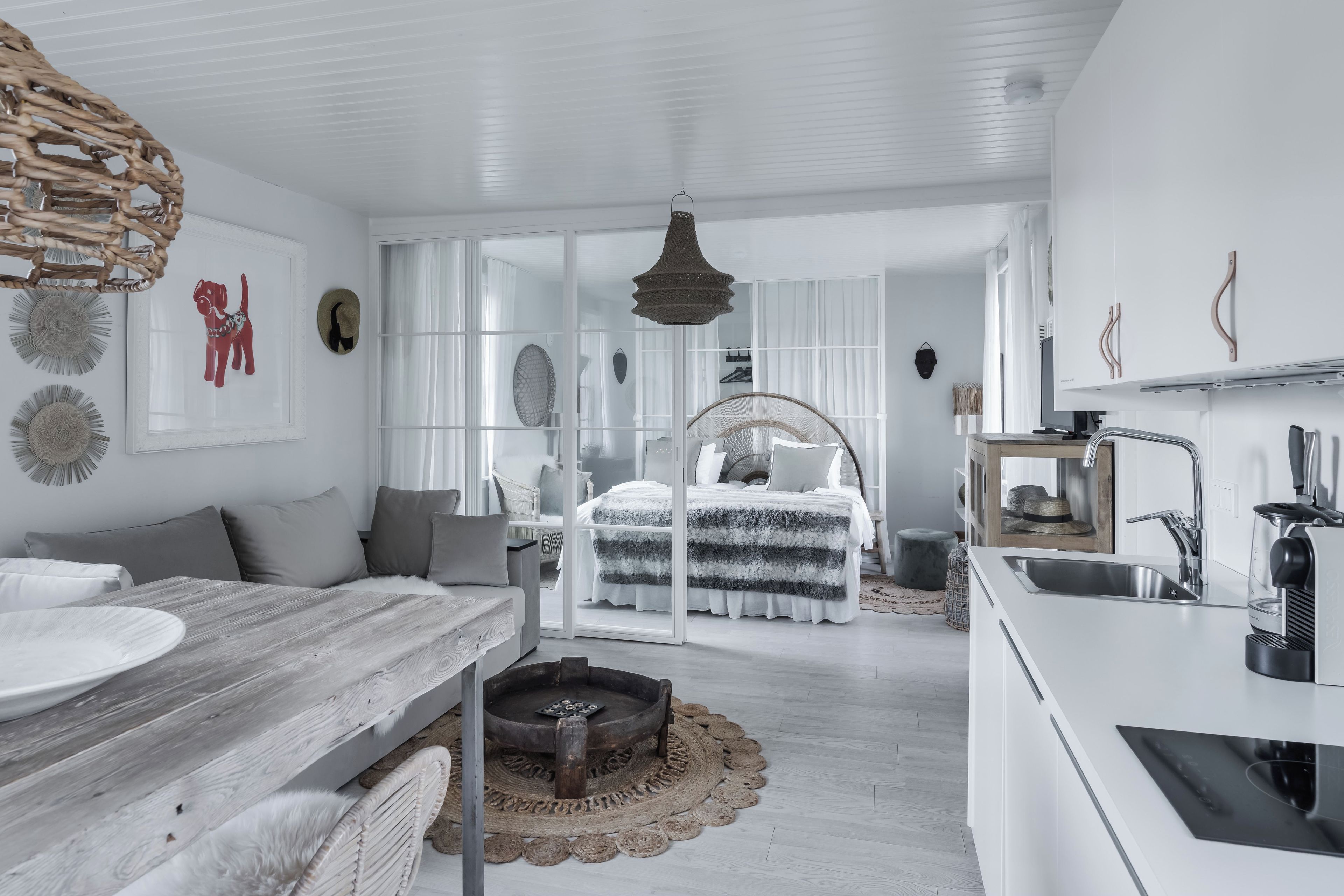 A modern, minimalist bedroom with a large bed, a separate sitting area, and a kitchenette.