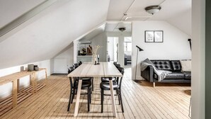 A spacious loft with a high ceiling, a dining area with a long table and chairs, a black leather sofa, and a wooden floor. - Pensionat Enehall (Bastad)