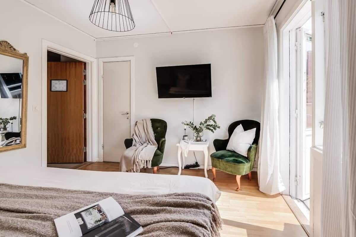 Ein modernes Hotelzimmer mit einem großen Bett, einem an der Wand befestigten Fernseher und zwei grünen Sesseln.
