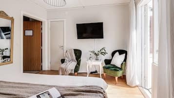 A modern hotel room with a large bed, a television mounted on the wall, and two green armchairs.