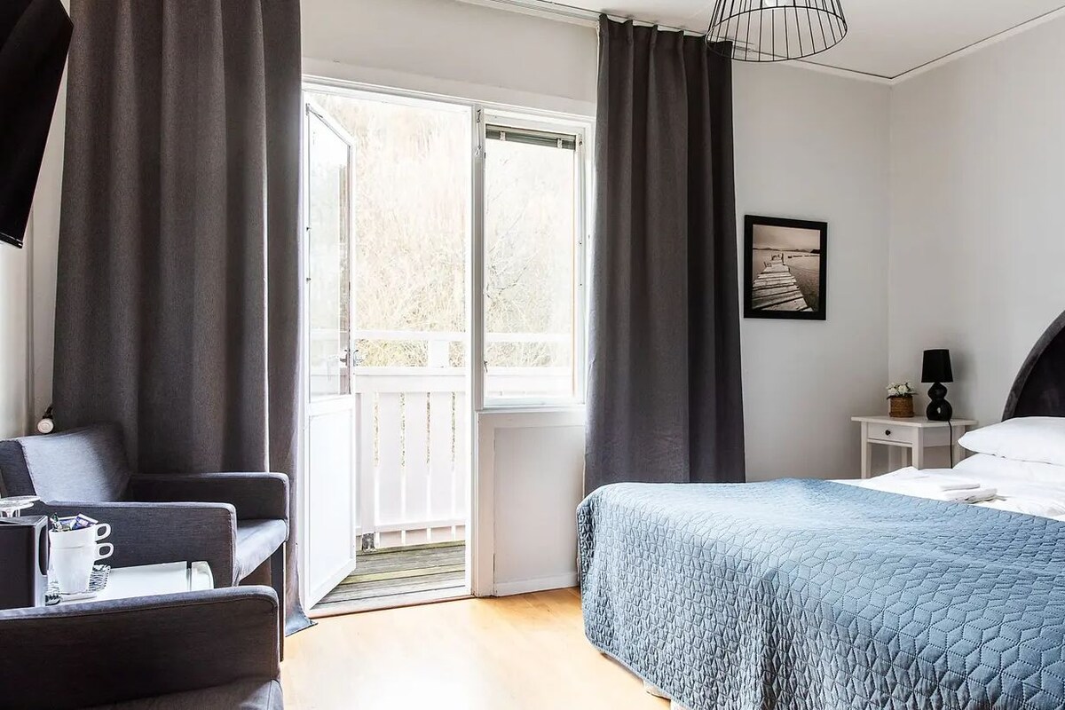 Un dormitorio con cama, una silla, una mesita de noche, una lámpara y un cuadro en la pared.