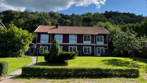 A two-story house with a red roof and white trim, surrounded by a well-maintained lawn and trees. - Pensionat Enehall (Bastad)