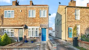 A narrow street with two brick houses, one with a blue door and the other with a white door.