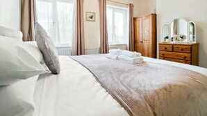 A bedroom with a bed, a dresser, a mirror, and two windows with curtains.