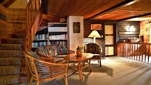 Interior acollidor d'una cabana de fusta, amb escala, sofà, taula i prestatgeria.