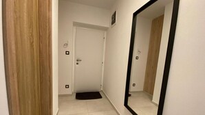A narrow hallway with a wooden door, a white door, and a large mirror on the wall.