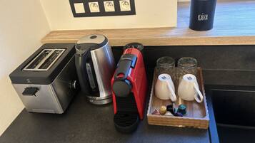 Un plan de travail de cuisine avec un grille-pain, une bouilloire, une cafetière rouge et un plateau contenant des théières et des tasses.