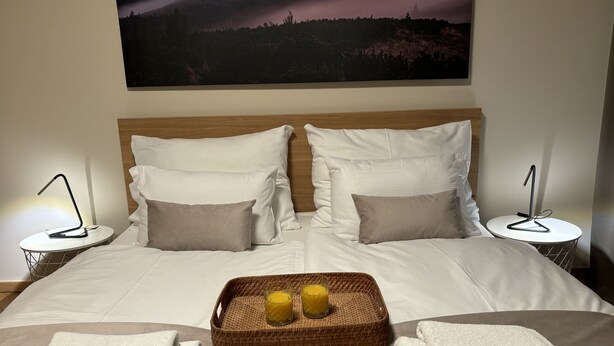 A neatly made bed with white linens, two pillows, a tray with two glasses of water, and two folded towels.