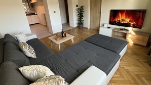 A modern living room with a sofa, a TV, a small table, and a potted plant.