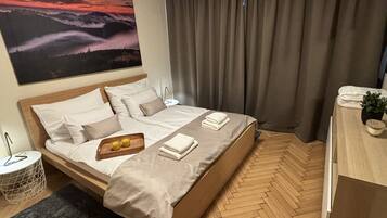 A neatly made bed with a wooden headboard, a bedside table with a lamp, and a large painting of a sunset on the wall.
