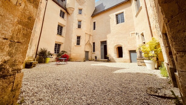 A courtyard with a cobblestone ground, a stone archway, and a building with multiple windows and a tower.