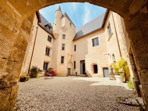 Un patio con suelo de piedra, un arco de piedra y un edificio con varias ventanas y una torre.