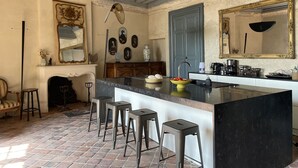 A kitchen with a marble island, bar stools, a fireplace, and various wall decorations.