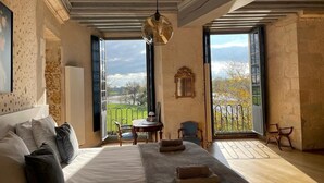 A bedroom with a large bed, a desk, and a view of a green landscape through open doors.