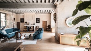 A spacious living room with a high ceiling, wooden beams, a fireplace, and a large plant.