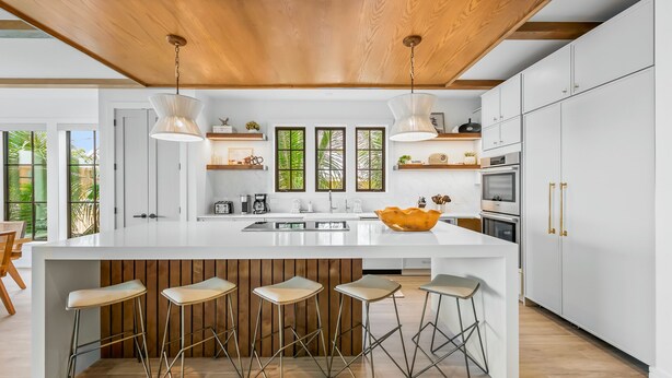 Una cocina moderna con una isla grande, taburetes de bar y vigas de madera en el techo.