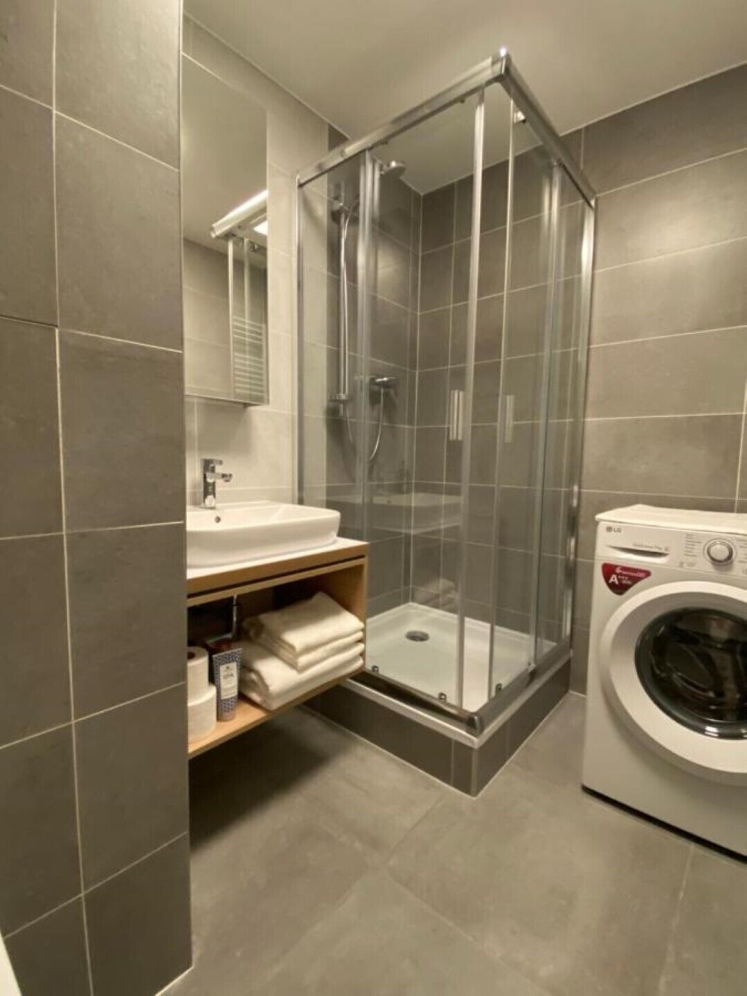 Ett modernt badrum med en duschavdelning med glasväggar, ett handfat, en spegel och en tvättmaskin.