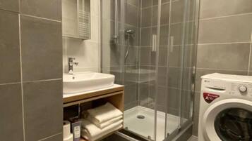Ett modernt badrum med en duschavdelning med glasväggar, ett handfat, en spegel och en tvättmaskin.