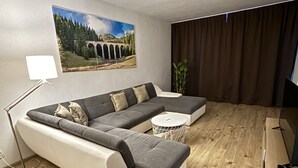 Una sala de estar moderna con un sofá modular, una pequeña mesa redonda, una lámpara de pie y un cuadro de un puente.
