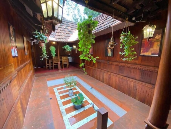 A traditional wooden interior with hanging plants, a central seating area, and a tiled floor.