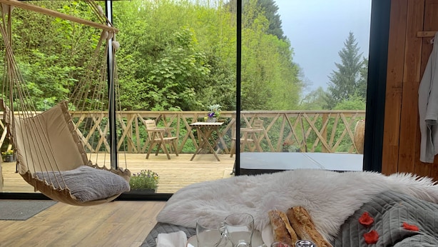 A bedroom with a large window, a hanging chair, a bed with a fluffy blanket, and breakfast items on the bed. - DOMAINE RÊVES ETOILÉS (La Roche-Maurice)