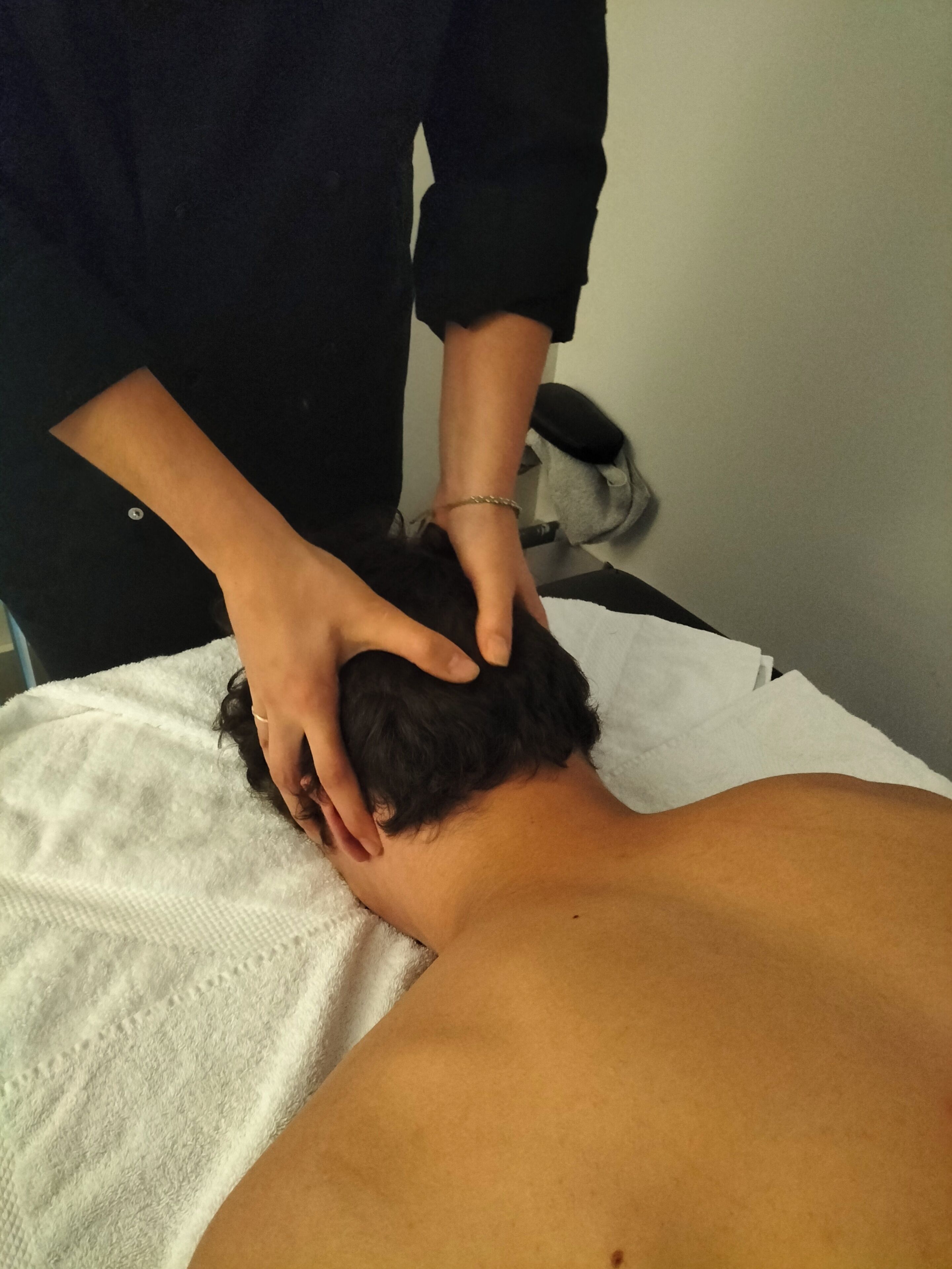 A person receiving a head massage on a white towel-covered surface.