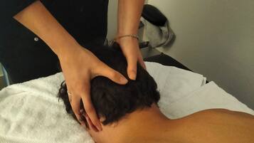 A person receiving a head massage on a white towel-covered surface.