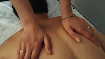 A person receiving a back massage on a bed with a white sheet.