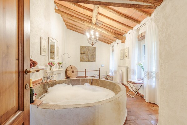 Un baño rústico con una amplia bañera de piedra, vigas de madera y un candelabro.