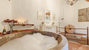 Ein rustikales Badezimmer mit einer Steinbadewanne, Holzregalen mit Toilettenartikeln und einem Vintage-Spiegel.