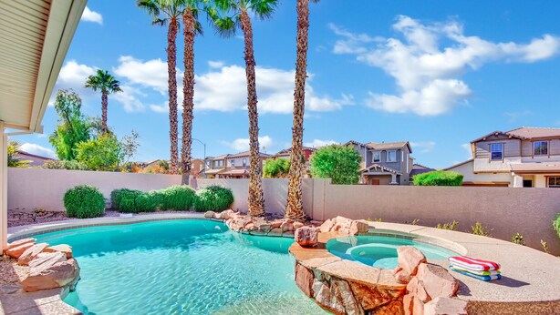 A swimming pool with a curved design, surrounded by rocks and palm trees. - Seven Palms Stylish Home with Pool, Hot Tub,& Movie Room (Henderson)