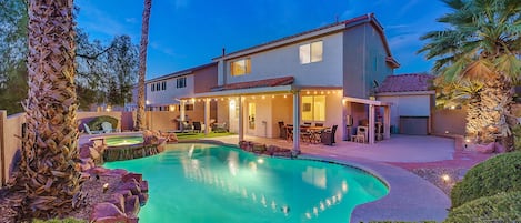 A two-story house with a swimming pool, outdoor furniture, and palm trees.