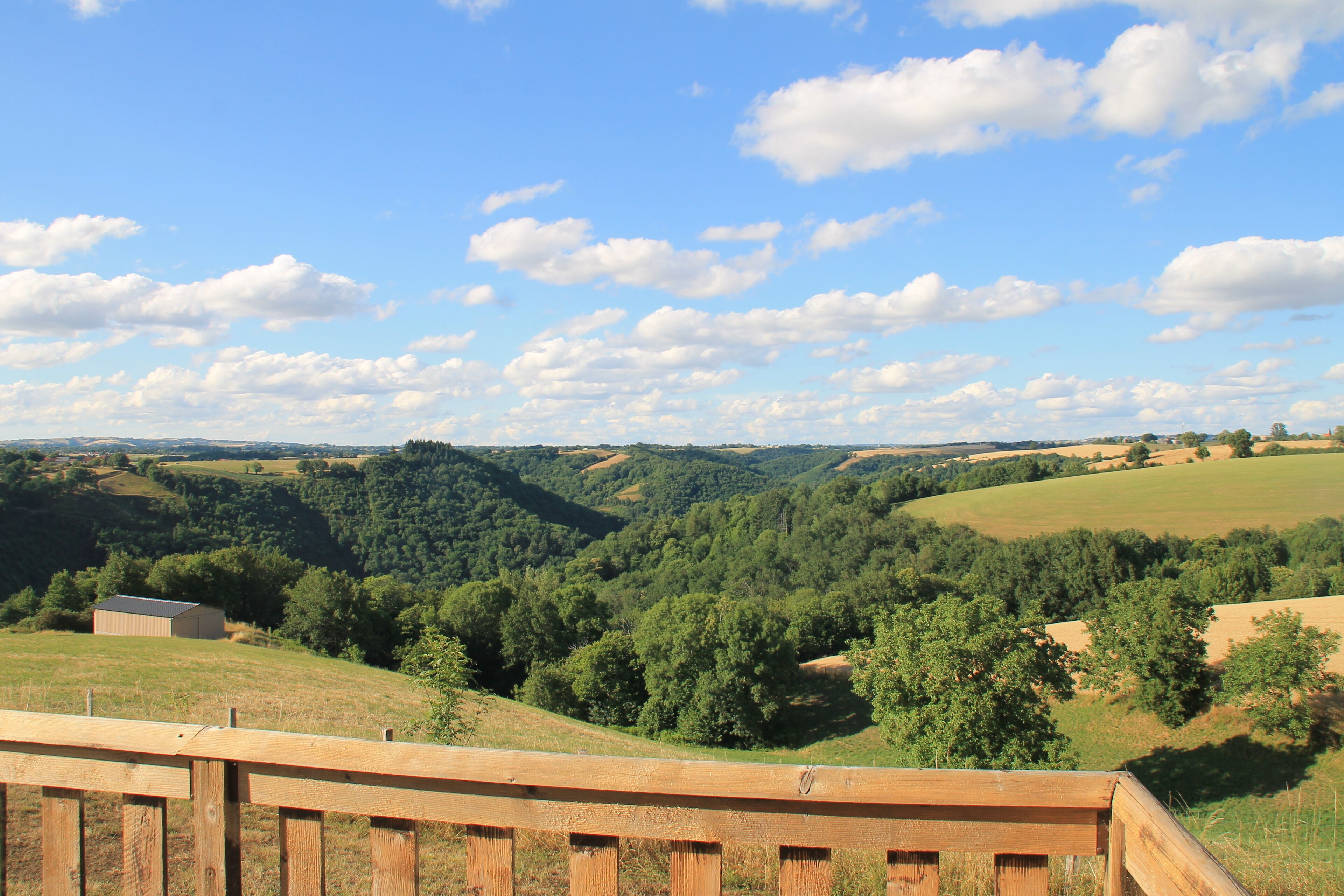 A scenic view from a wooden deck overlooking rolling hills and a small building in the distance.